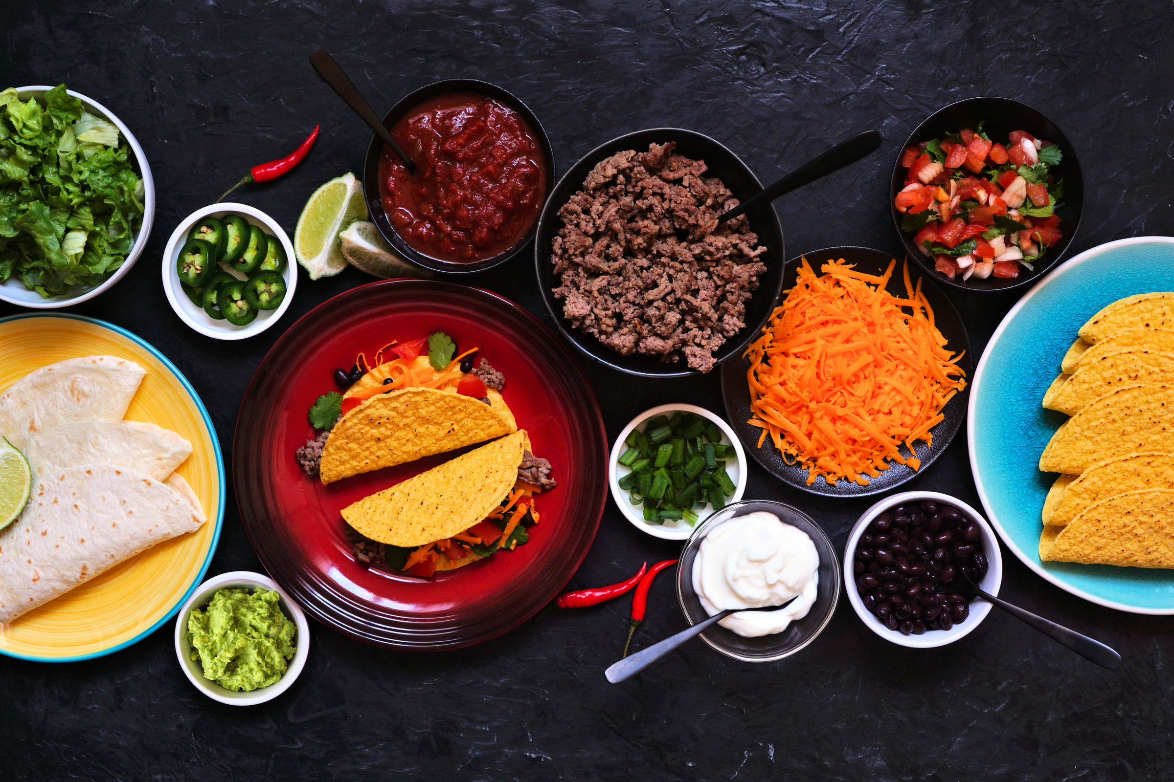 Taco bar table scene with a variety of ingredients on a dark slate background